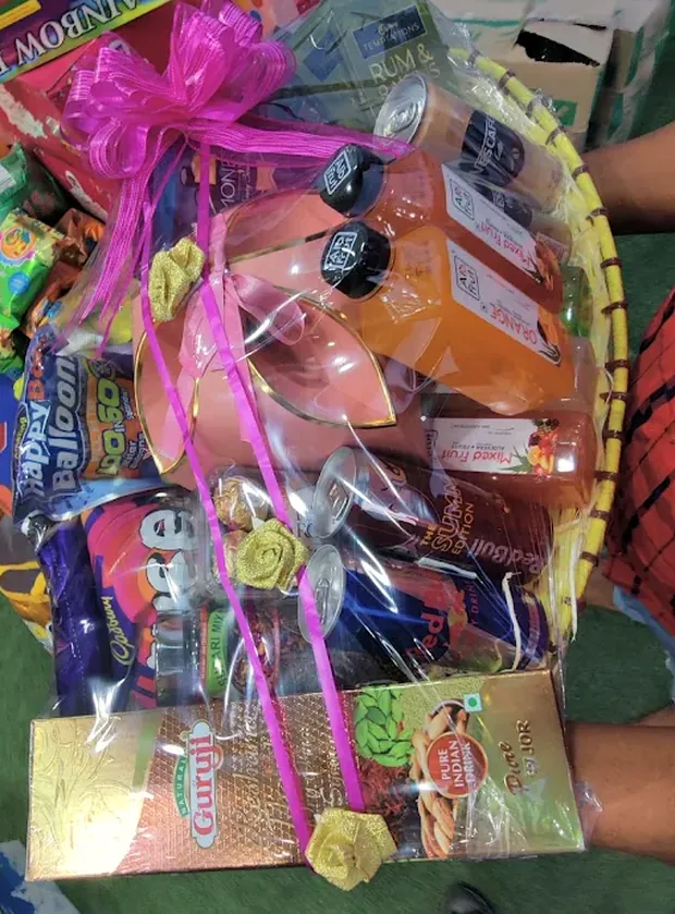 A festive hamper basket wrapped in cellophane with a pink ribbon, packed with drinks, chocolate and snacks