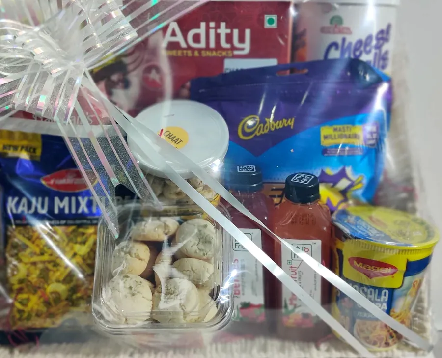 A hamper tray of kaju mixture, biscuits, chocolate and boxed sweets under cellophane