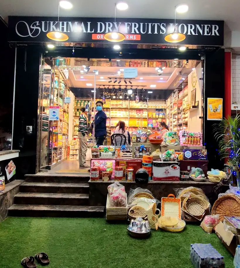 Sukhmal Dry Fruits Korner lit up after dark, with gift hampers and baskets stacked on the step outside