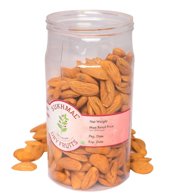 A clear jar of whole almonds with a pink Sukhmal Dry Fruits label, almonds spilled around its base